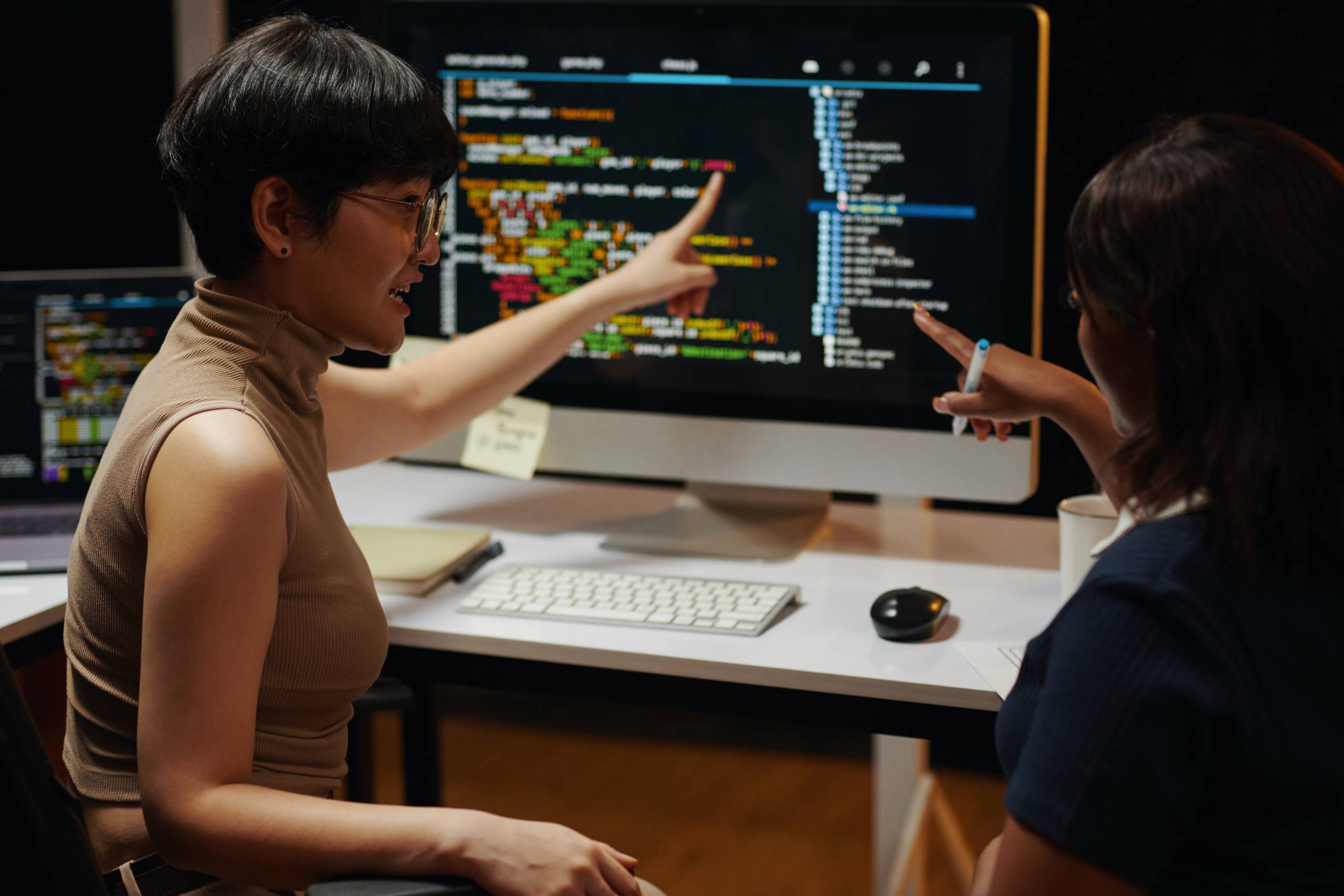 Female developers discussing programming code on computer screen